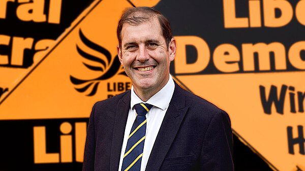 Lee Dillon stood in front of giant correx diamonds that say "Liberal Democrats"
