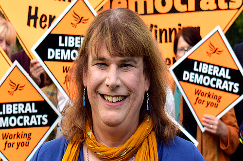 Helen Belcher stood in front of a group of Liberal Democrats holding orange correx diamonds that read "Liberal Democrats"