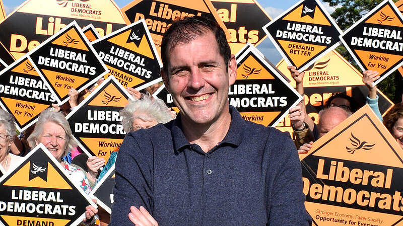 Lee Dillon stood in front of a group of Liberal Democrats holding orange correx diamonds that read "Liberal Democrats" on them